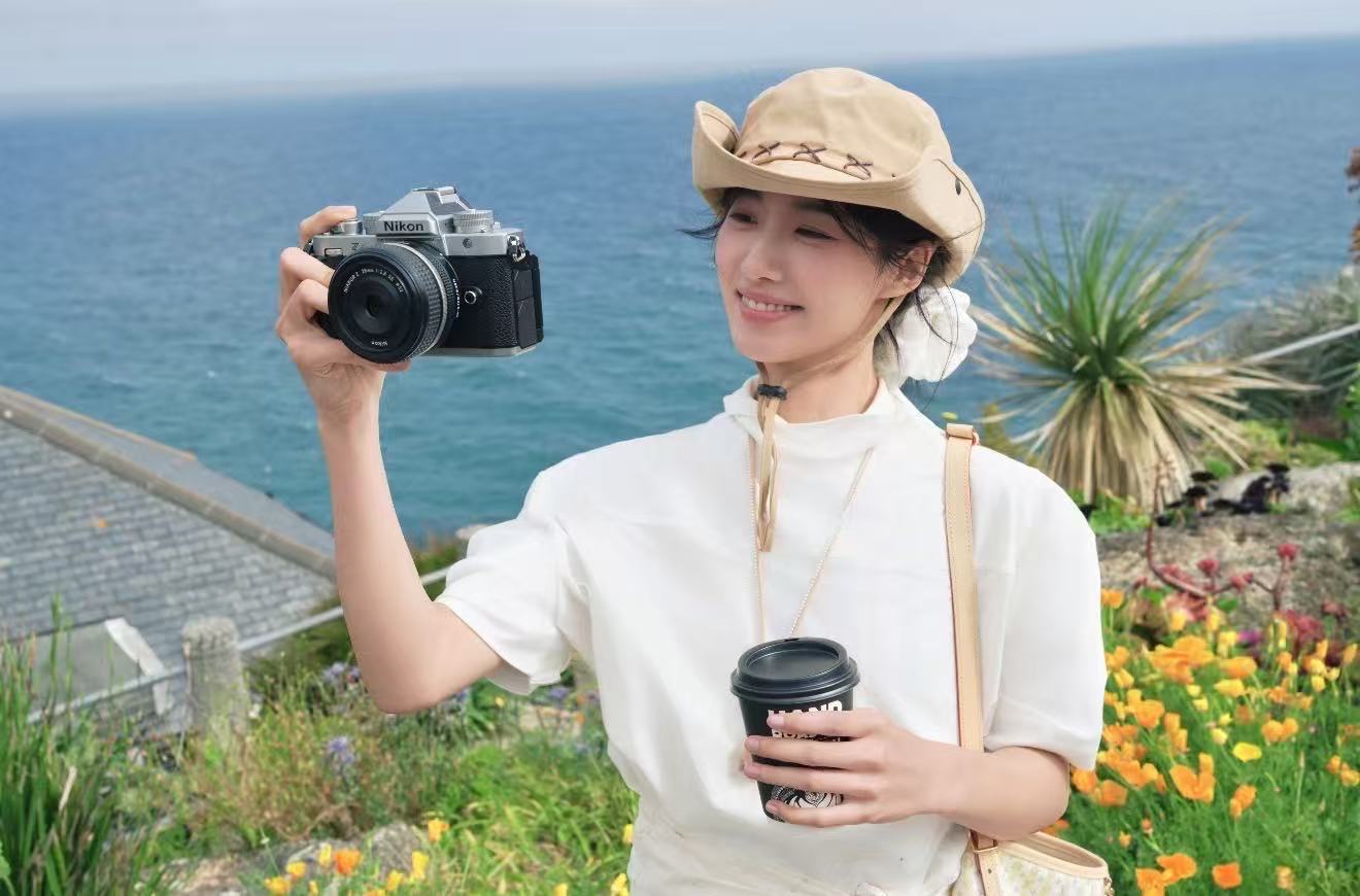 A person in a white shirt holding a film camera above a blue sea
